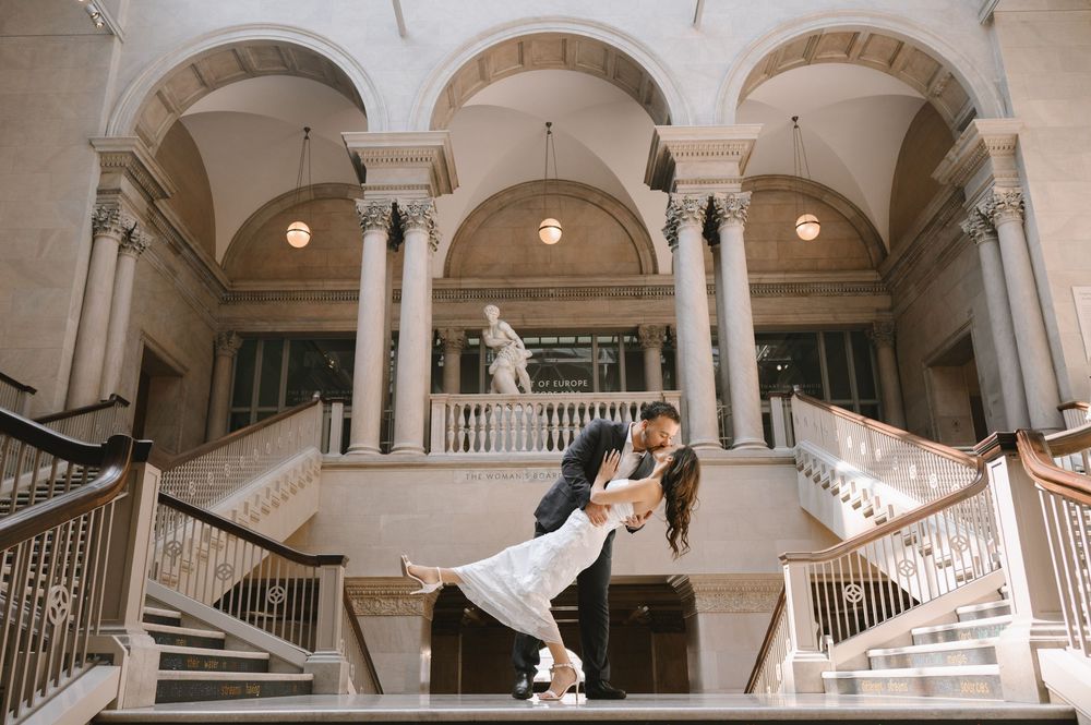 Couple sharing a romantic dip kiss on grand staircase in elegant neoclassical wedding venue with tall columns.