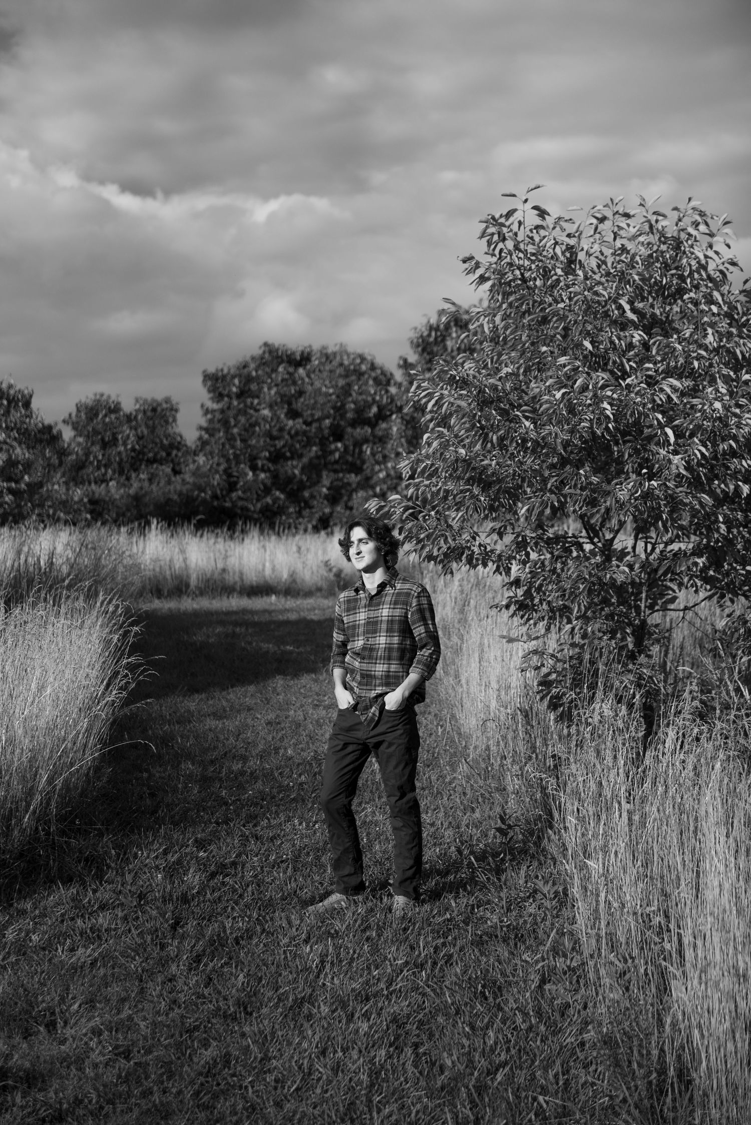 Black and white portrait in natural setting with tall grass and trees.