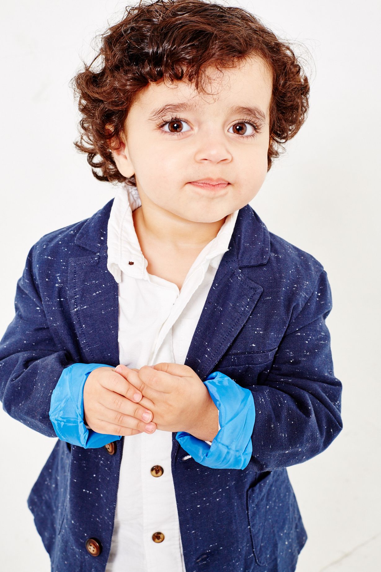 Young child in navy blazer and white shirt smiling at camera against white background.