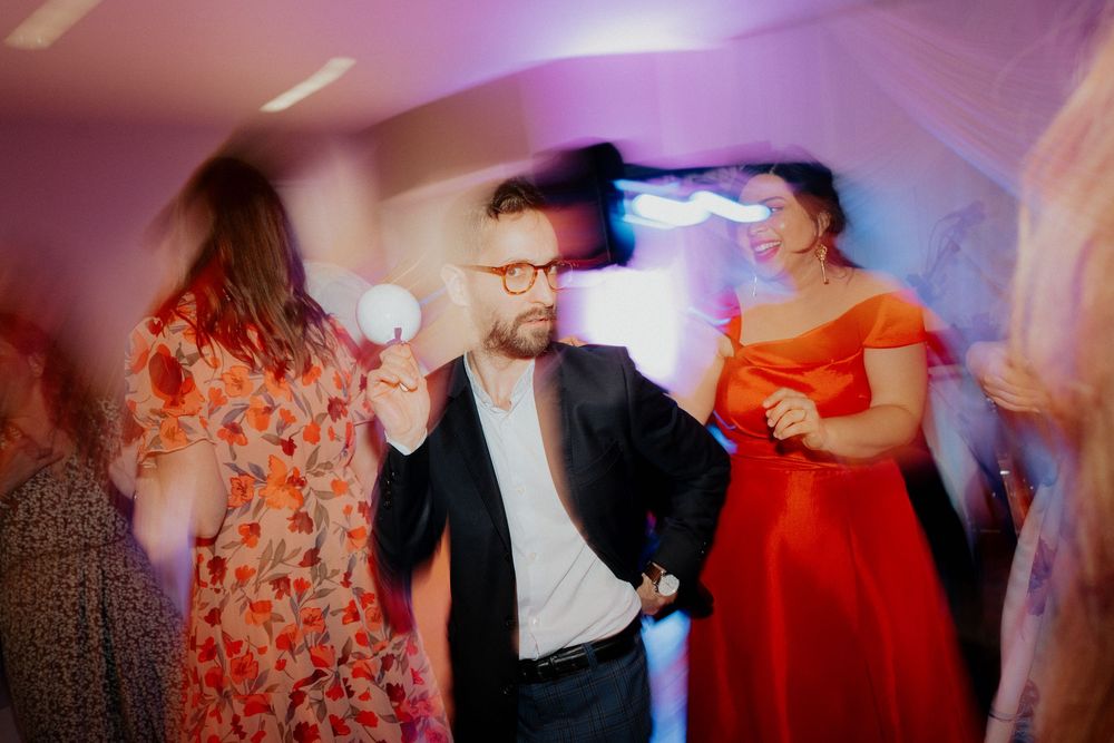 People dancing energetically at a wedding reception party with colorful lights and motion blur effect.