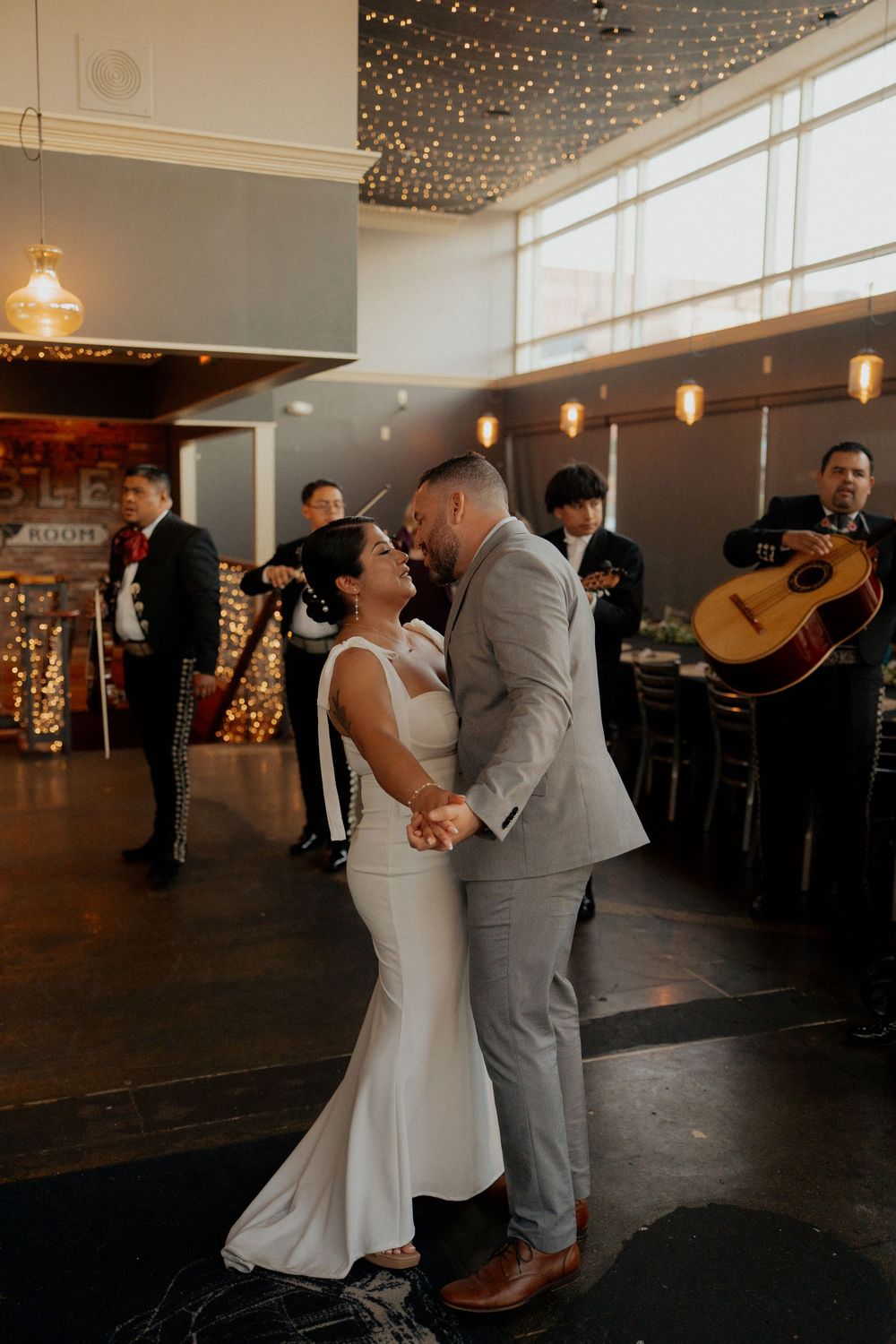 Bride and groom share first dance with mariachi band performing in background at elegant wedding reception.