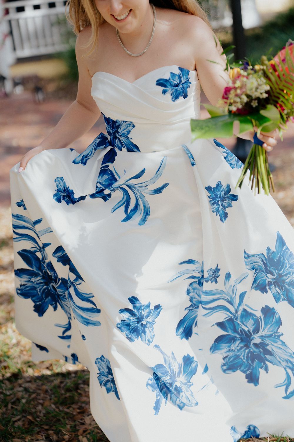Bride in a white strapless wedding gown with blue floral print holds bouquet outdoors.