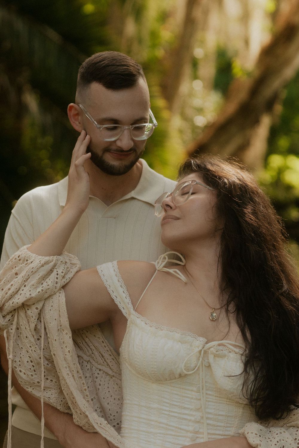 Romantic couple in white outfits sharing a tender moment outdoors, woman touching man's face gently.
