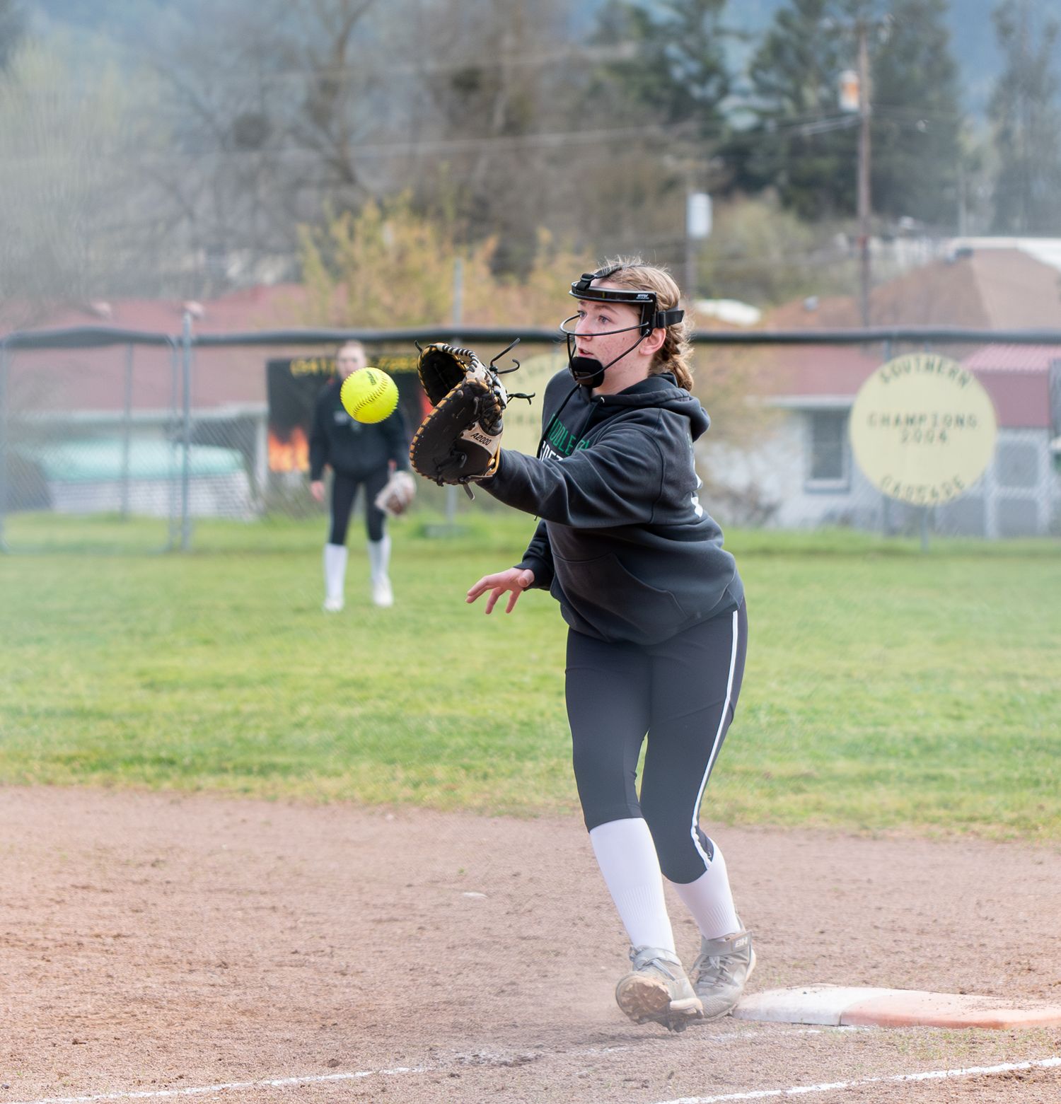 Softball player practicing fielding drills with bright yellow ball on dirt infield.