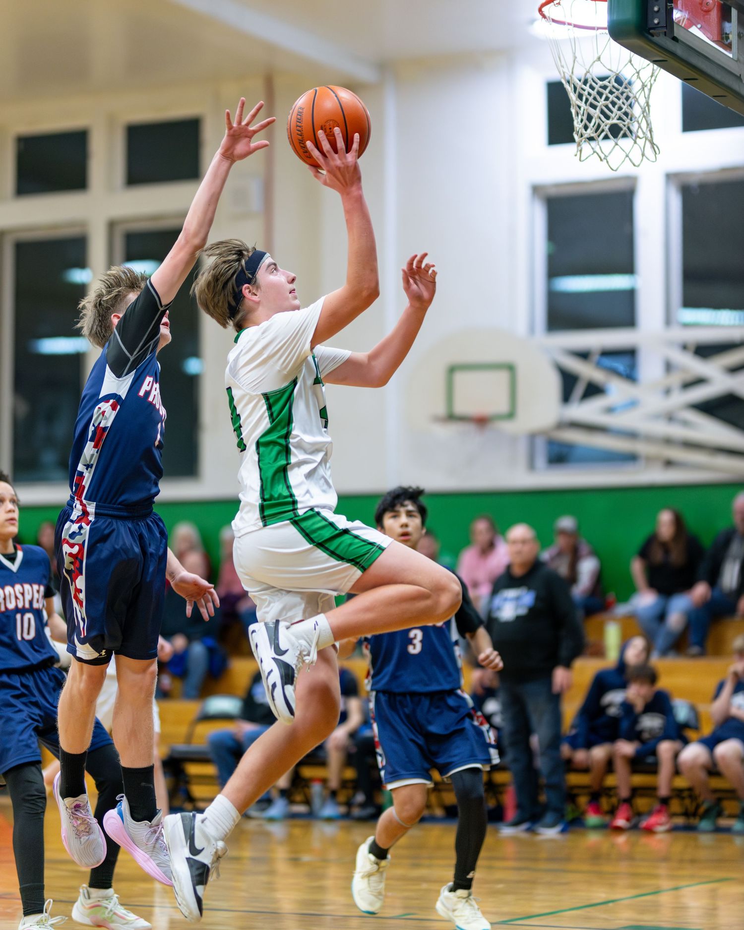 Basketball players battle for a rebound during an intense game in a high school gymnasium.