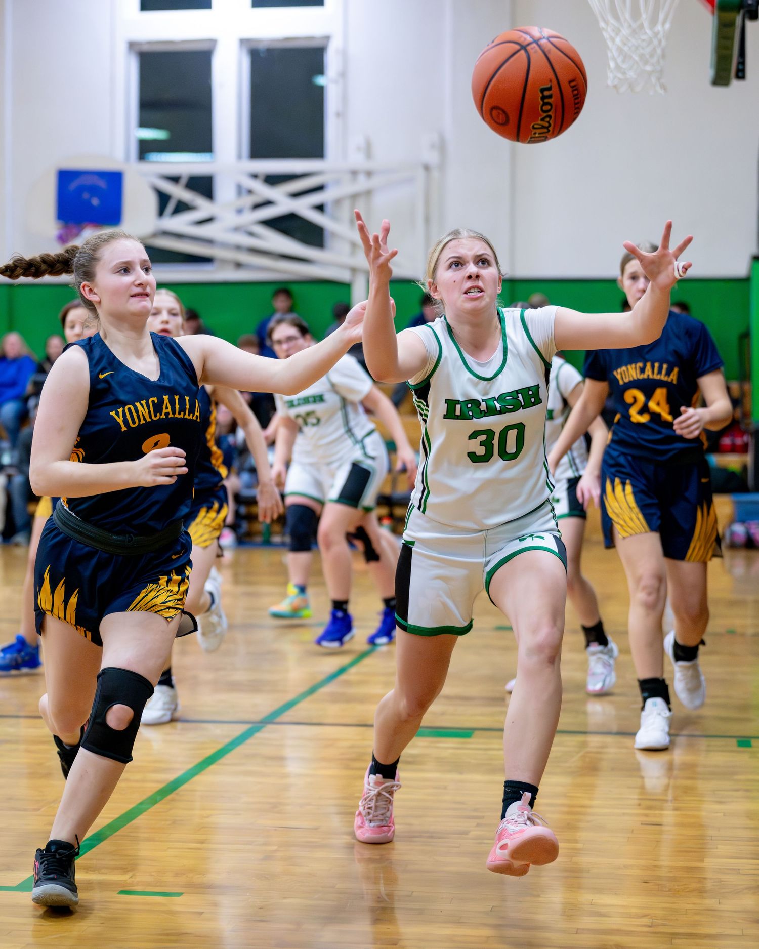 Basketball players dive and stretch to catch a loose ball during an intense game on a gymnasium court.