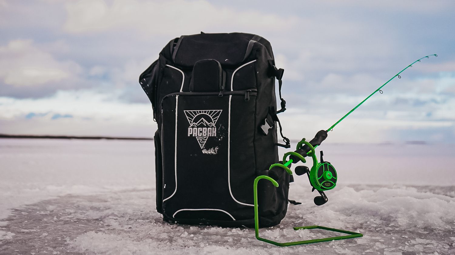 Ice fishing setup with black cooler and green fishing rod against snowy landscape.