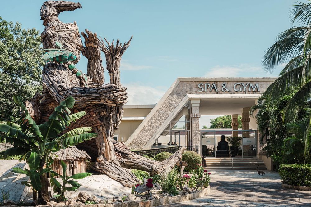 Large driftwood sculpture outside a tropical plaza entrance with palm trees, Sandos Caracol Wedding.