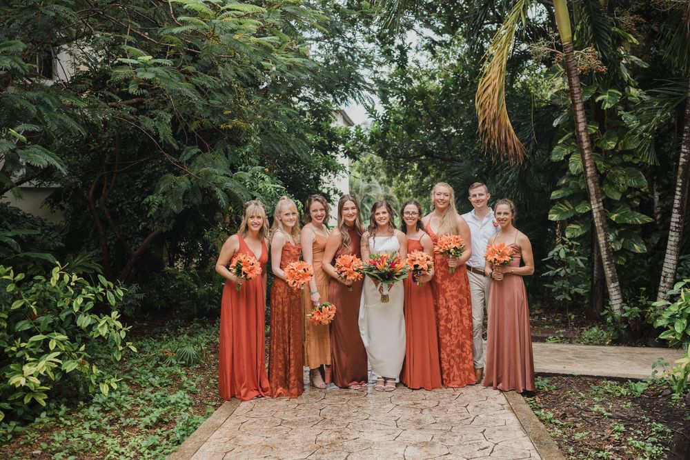 Wedding party in coral and peach dresses poses on a garden path surrounded by lush foliage, Sandos Caracol Wedding.