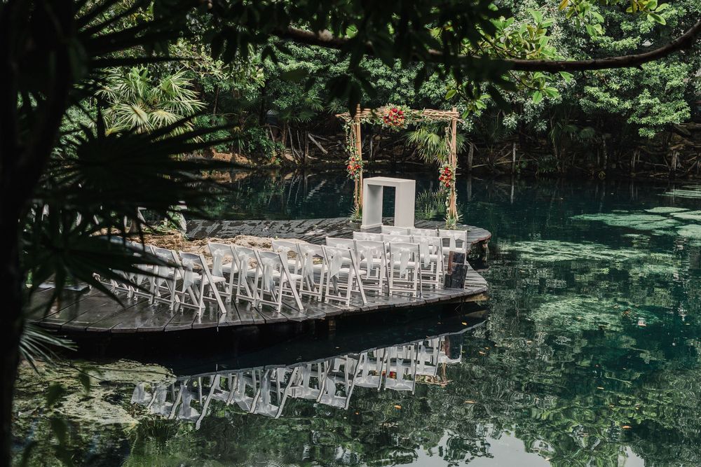 Outdoor wedding ceremony setup with white chairs beside a reflective pond in a tropical garden, Sandos Caracol Wedding Cenote.