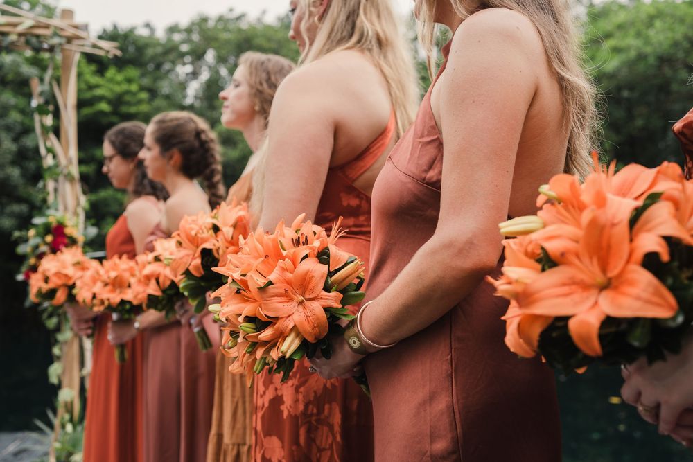 Bridesmaids in rust-colored dresses holding vibrant orange lily bouquets during an outdoor wedding ceremony, Sandos Caracol Wedding.