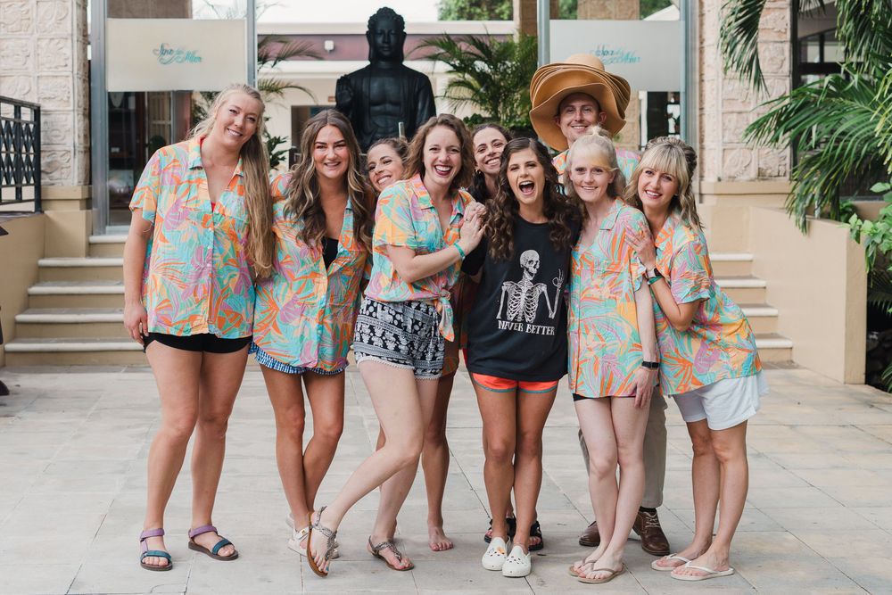 Group photo of friends in matching pastel outfits posing together at a resort entrance, Sandos Caracol Wedding.