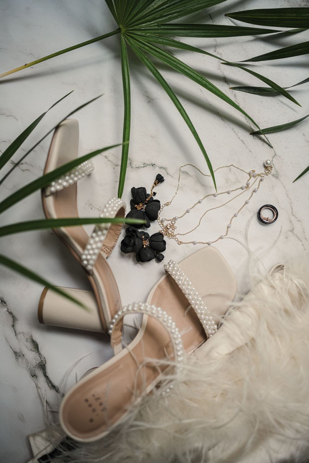 Wedding accessories including pearl-decorated heels, palm leaves, and black floral details on marble, Sandos Caracol Wedding.