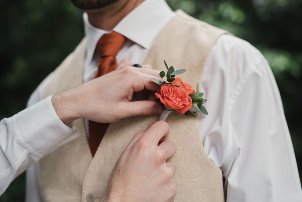 Close-up of hands pinning a coral rose boutonniere on a beige vest, Sandos Caracol Wedding.