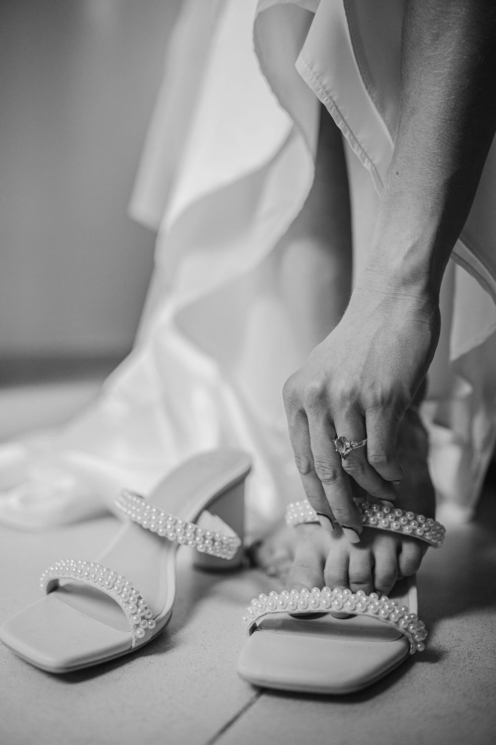 Black and white photo of bride putting on pearl-decorated wedding sandals, Sandos Caracol Wedding.