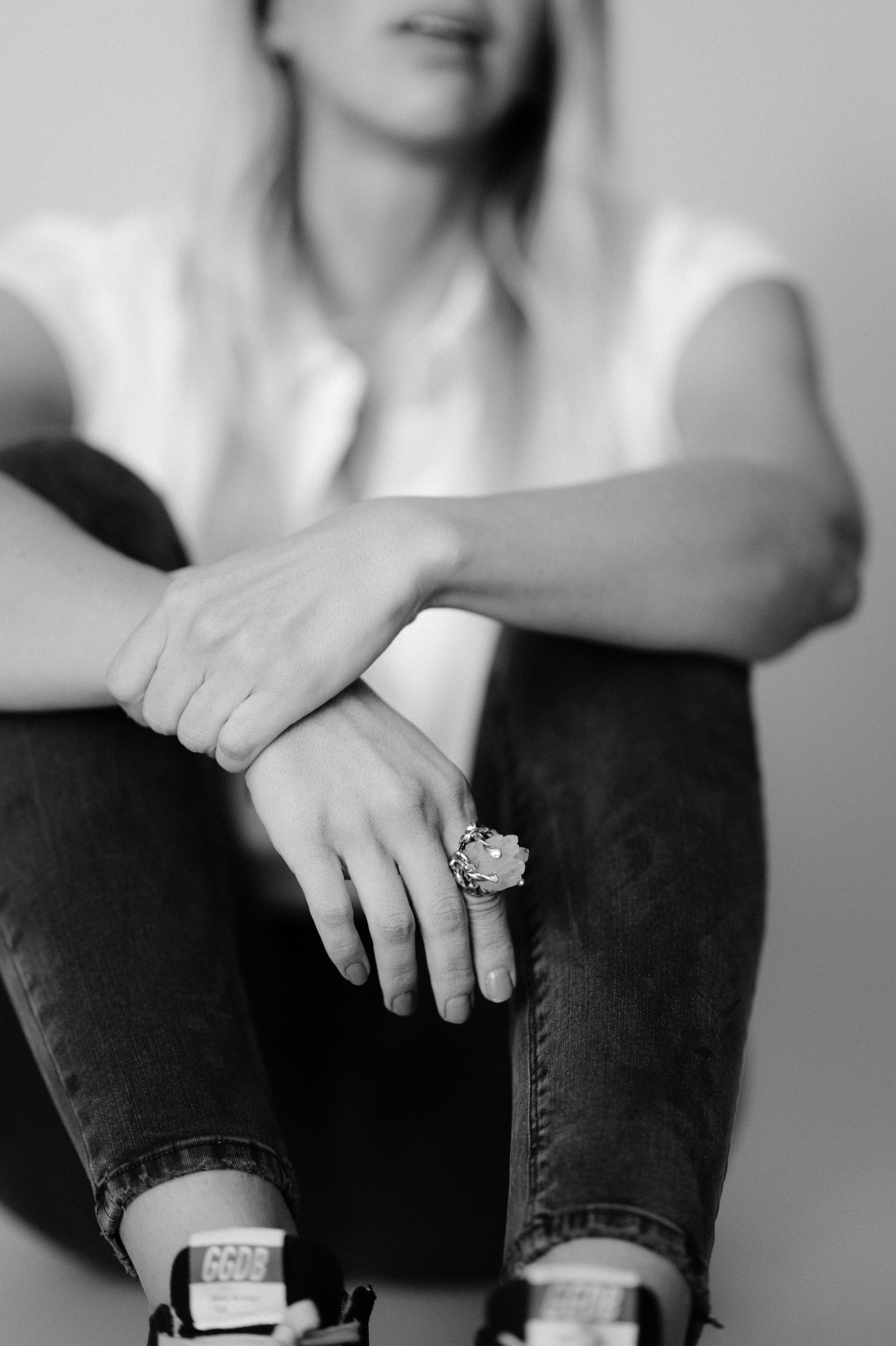 Black and white portrait focusing on hands with a statement ring while sitting in casual attire.