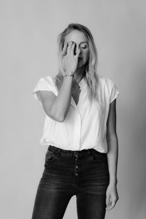 Minimalist portrait of someone in casual attire covering their face with one hand.