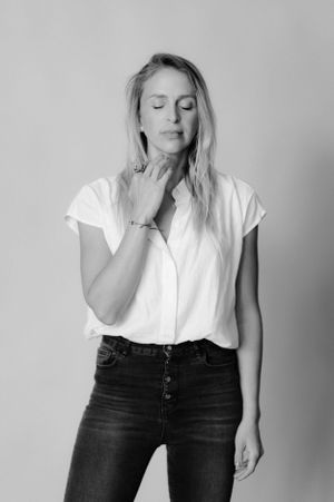 Black and white photo of person touching neck wearing casual white shirt and dark jeans.