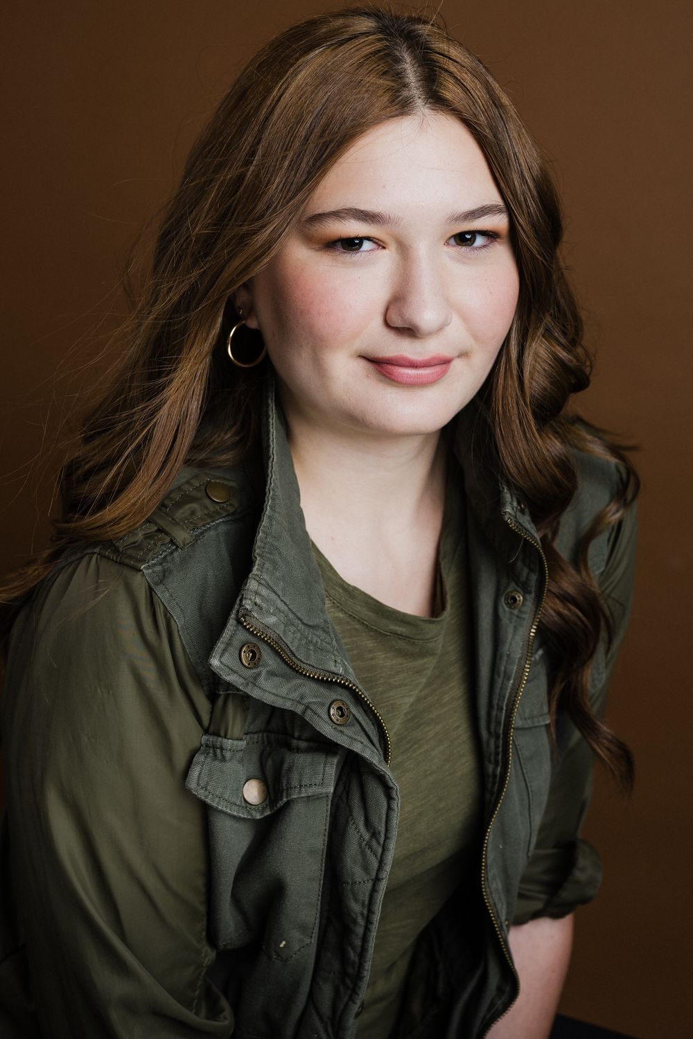 A series of four portrait photos showing someone in an olive green jacket and dark top against a brown backdrop.