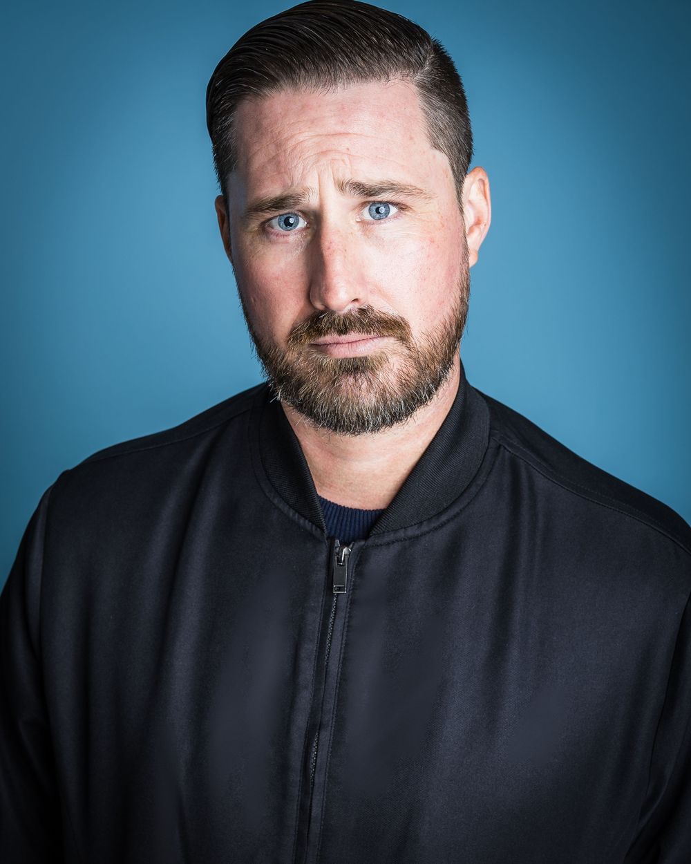 Portrait in black shirt against blue background showing different facial expressions and angles.
