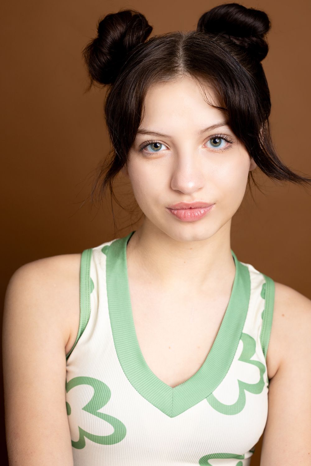 A series of identical portrait shots of someone wearing a white and green patterned sleeveless top against a brown backdrop.
