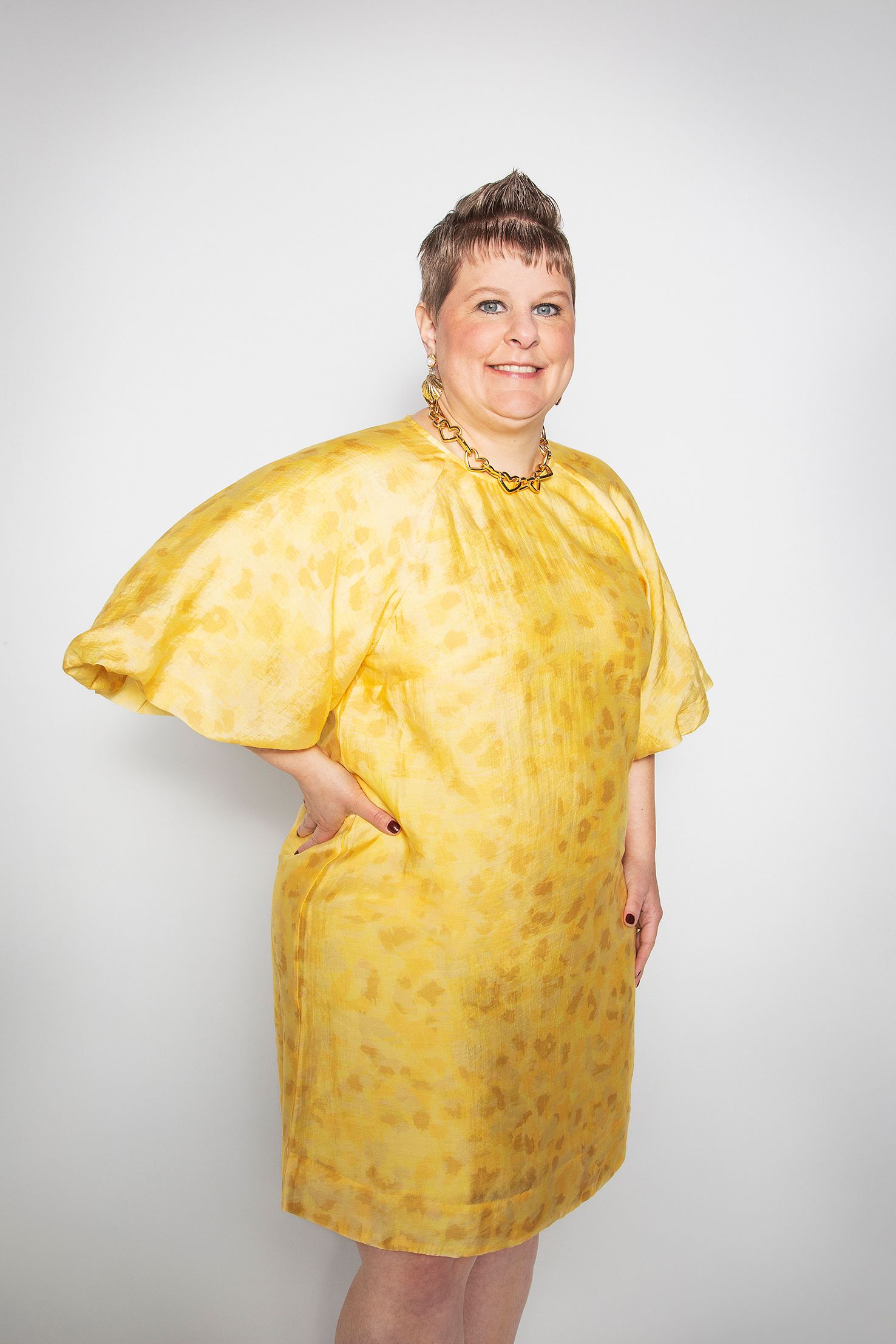Person wearing flowing yellow polka dot dress against white background.