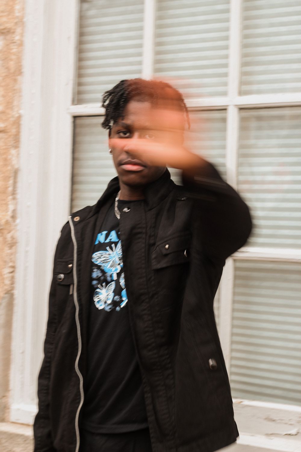 Photo of a man dressed in black, with his hands stretched and blocking his face from the picture.
