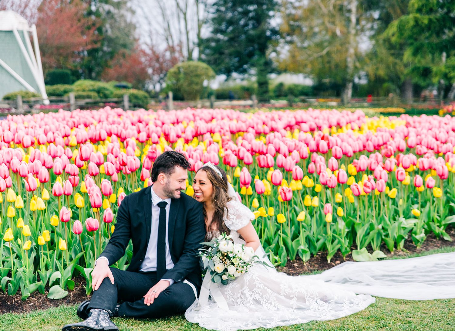 Couple poses among colorful spring tulip garden during wedding photoshoot.