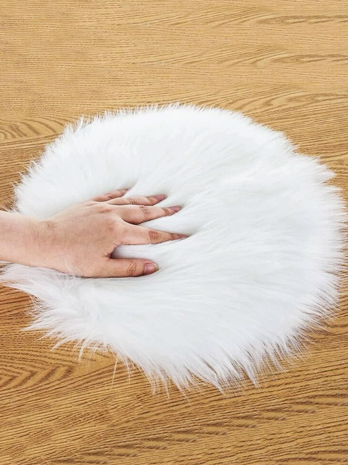 White fluffy faux fur rug displayed on wooden floor with hand touching surface.