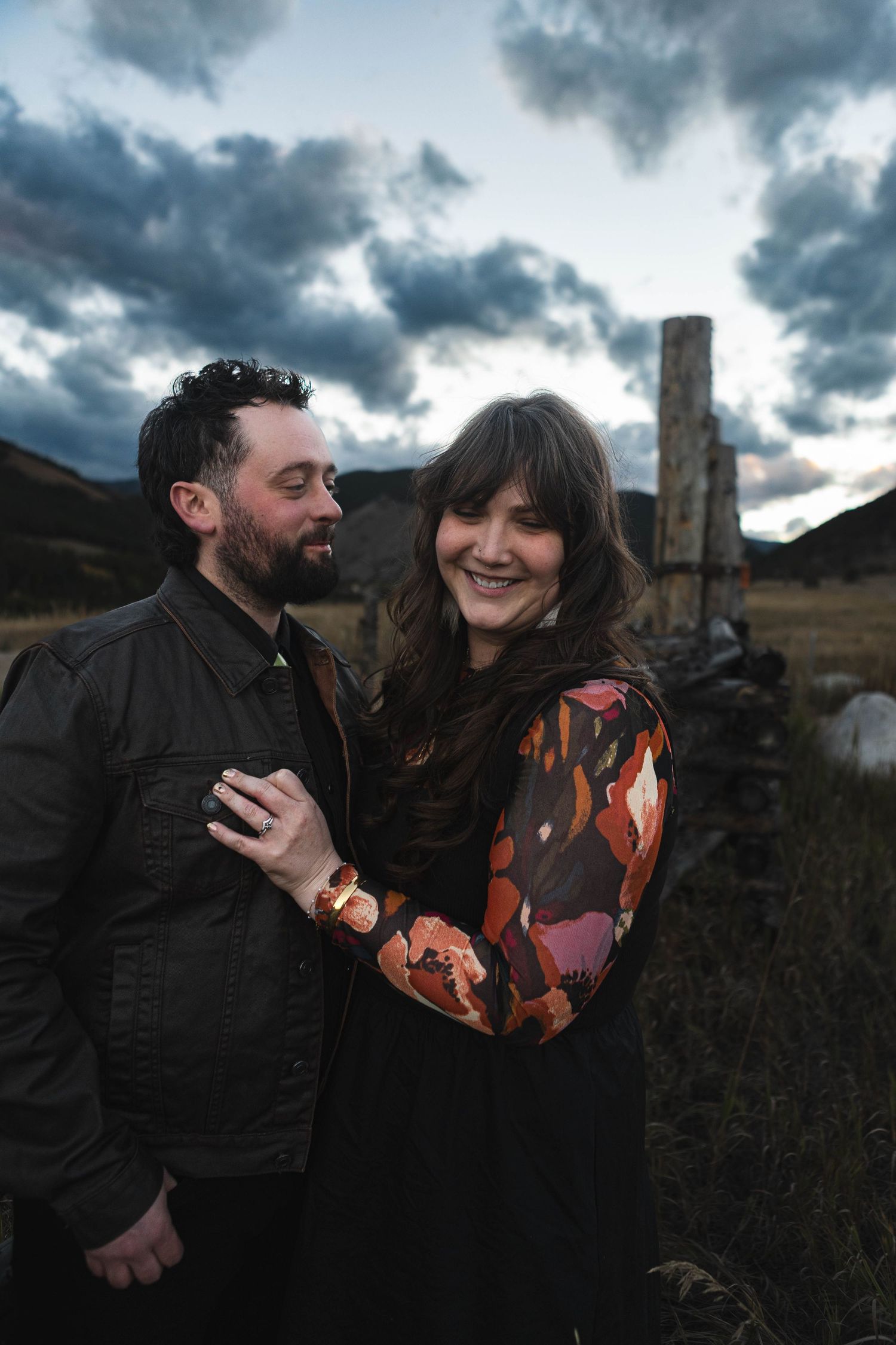 A couple shares a joyful moment together outdoors against a dramatic cloudy sky at sunset.