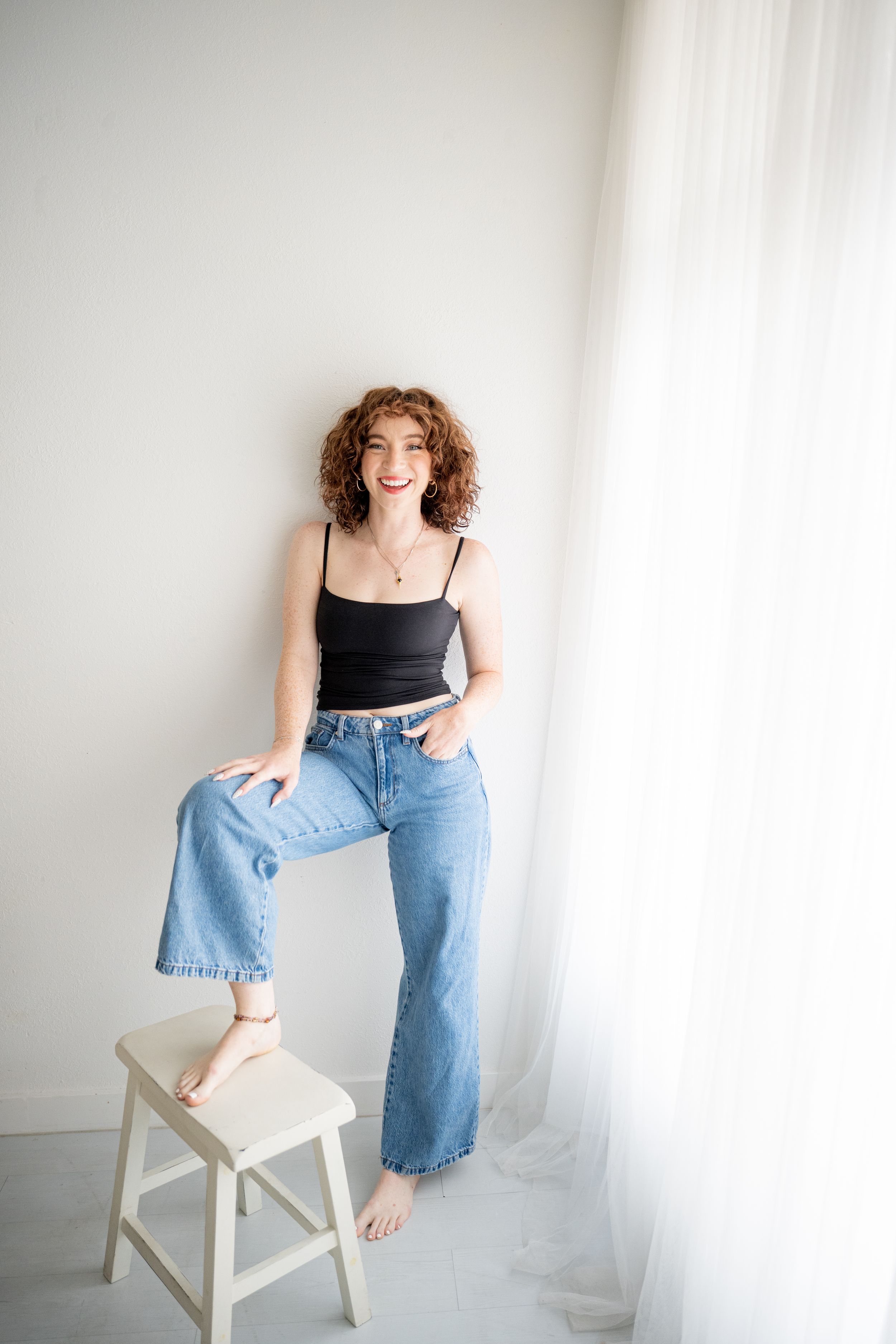 Person with wavy hair wearing white button-down shirt poses against dark wall.