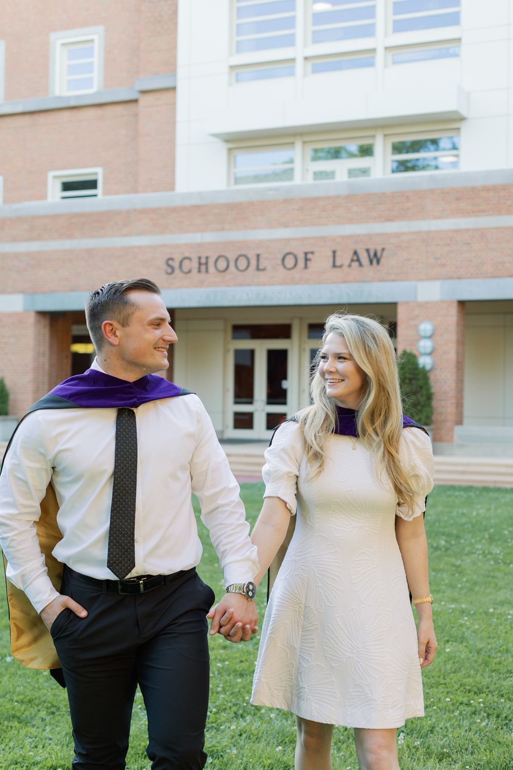 Graduates share a candid moment on the grass in front of their law school building.
