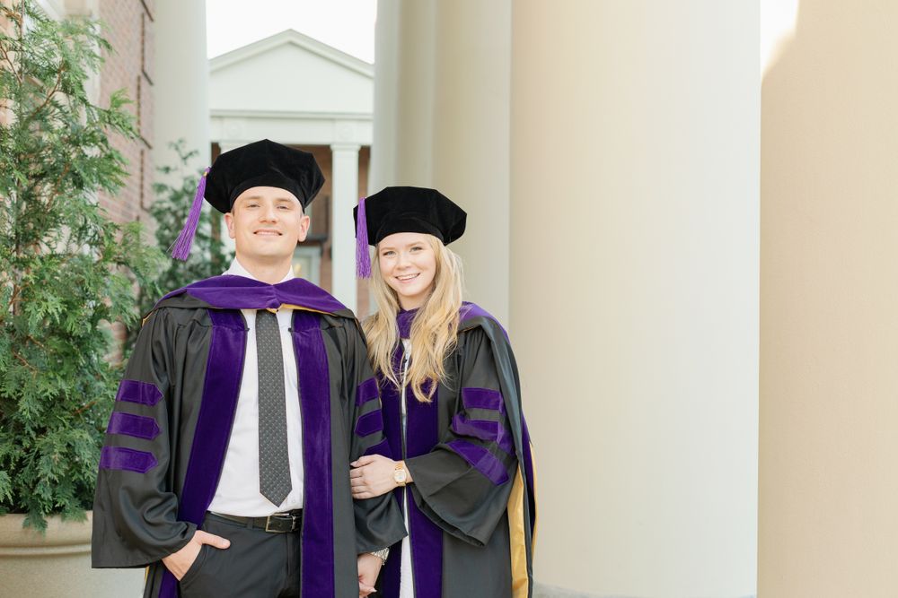 Law school graduates in academic regalia pose for photos between white columns.