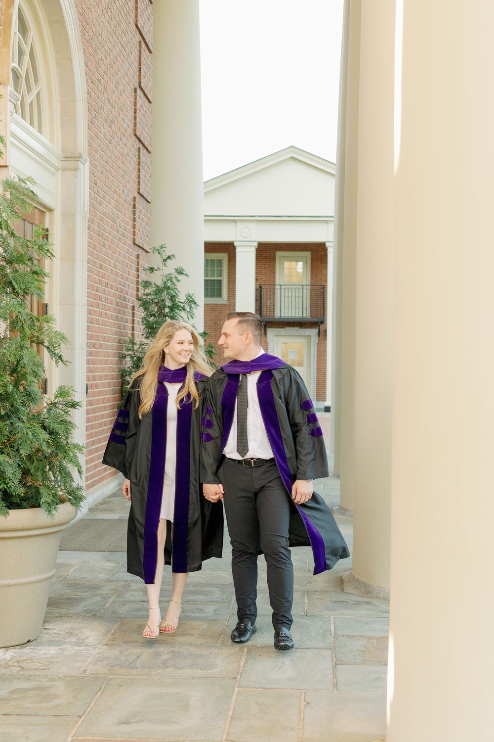 Graduates share a romantic moment while walking through a columned walkway.