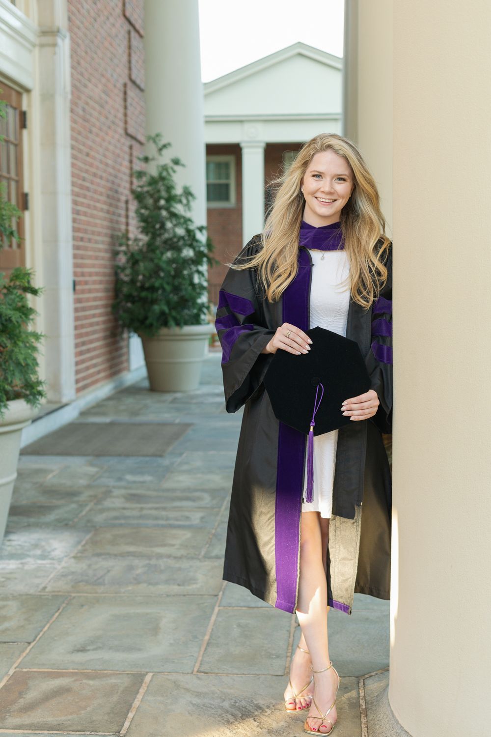 Graduate in academic regalia poses playfully between columns at law school.