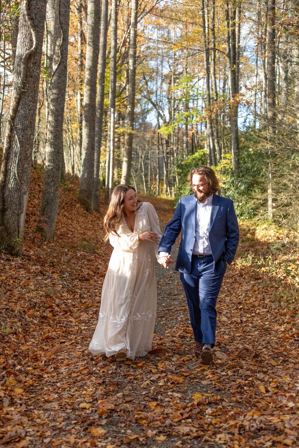 Playful couple walking through fallen autumn leaves in wooded area.
