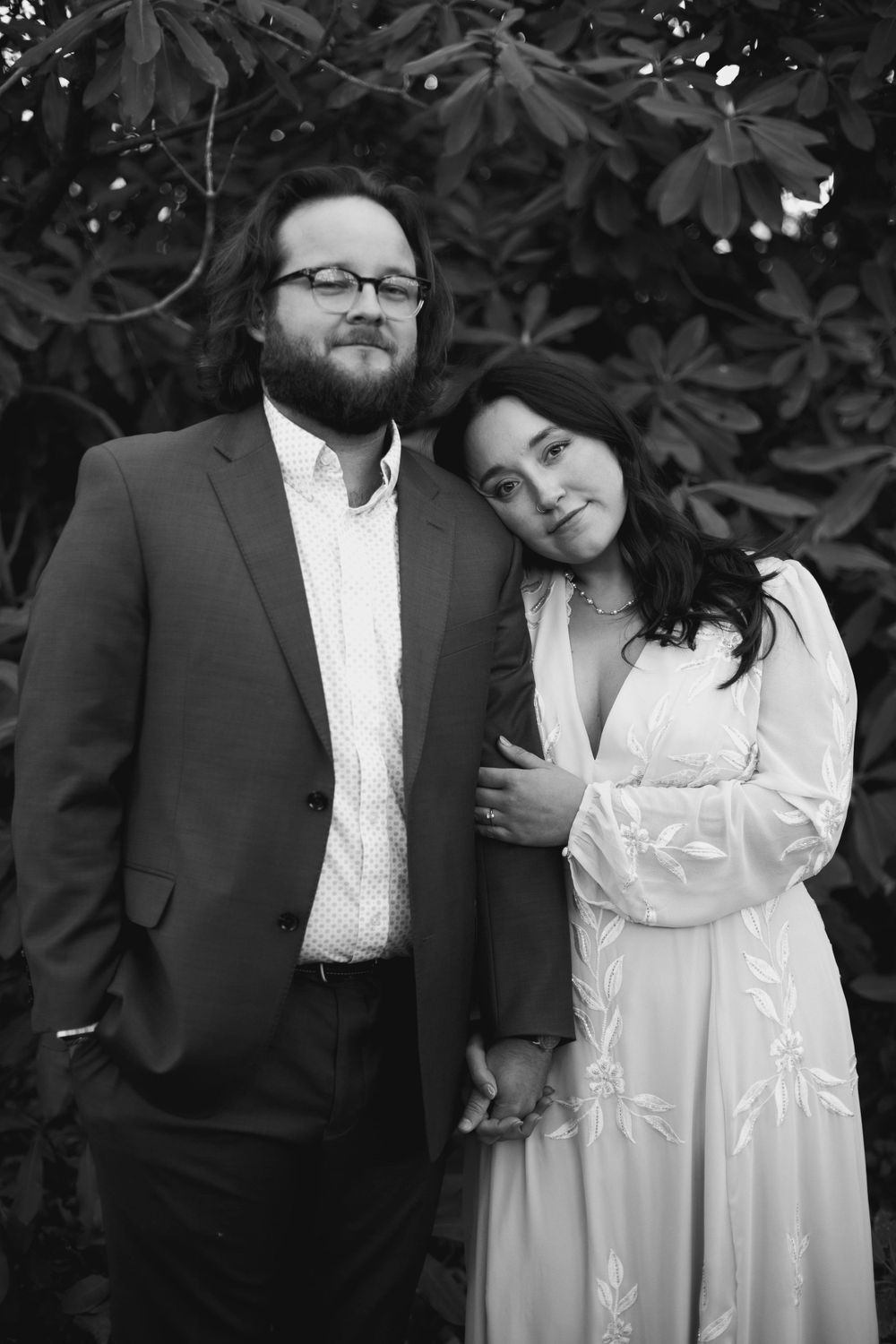A romantic couple poses together in formal attire against a dark foliage background.