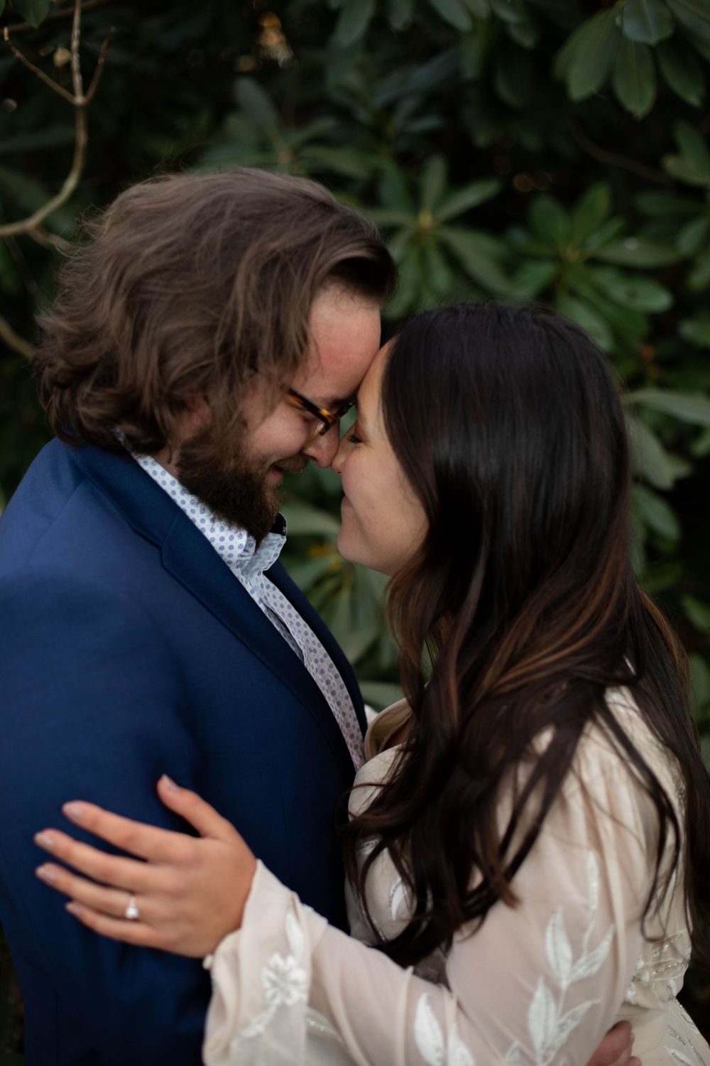 Romantic moment between couple in formal attire against green foliage background.