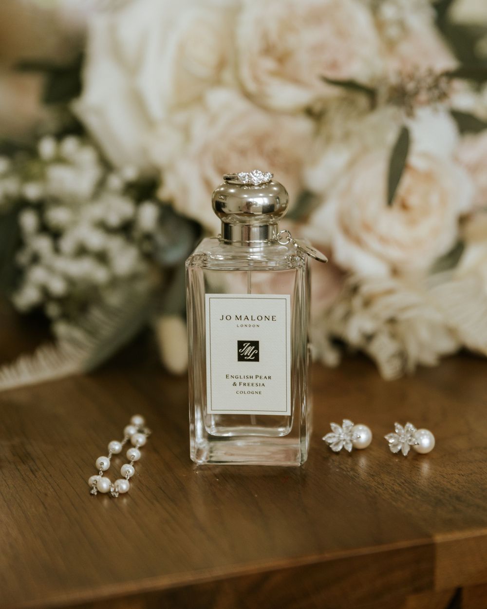 Wedding day perfume bottles and delicate white flowers arranged on wooden surface.