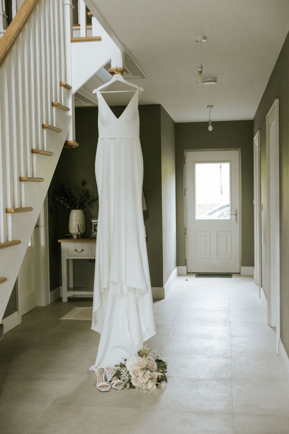 White wedding dress hanging in a minimalist hallway with natural light.
