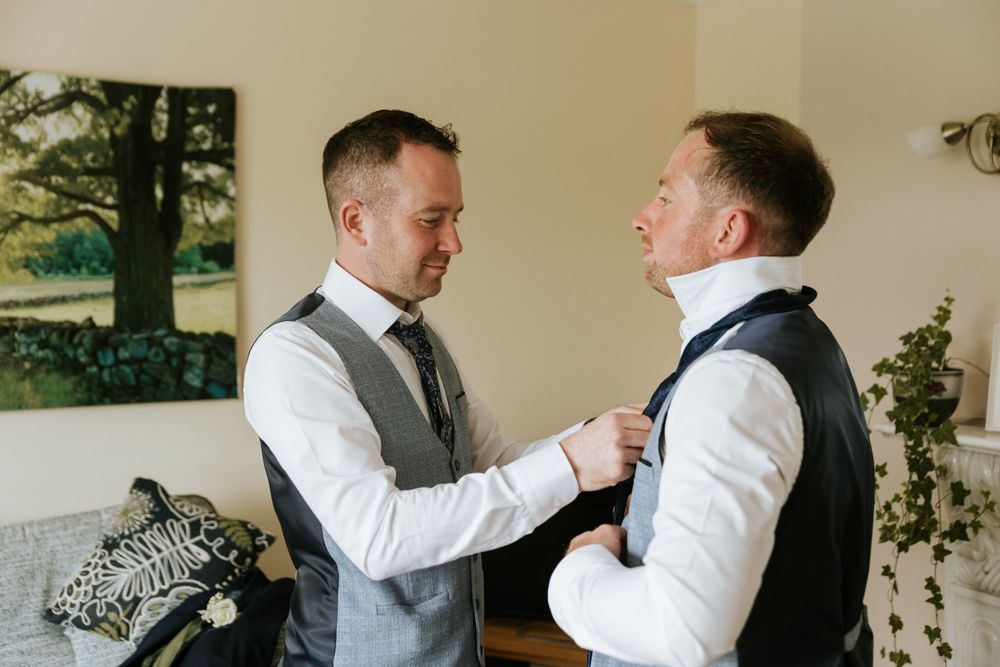 Groomsmen in formal attire help adjust ties and collars during wedding preparations.