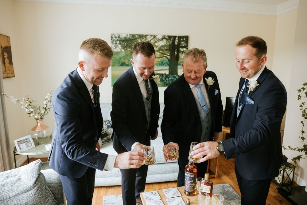 Groomsmen in navy suits gather for drinks and conversation indoors.