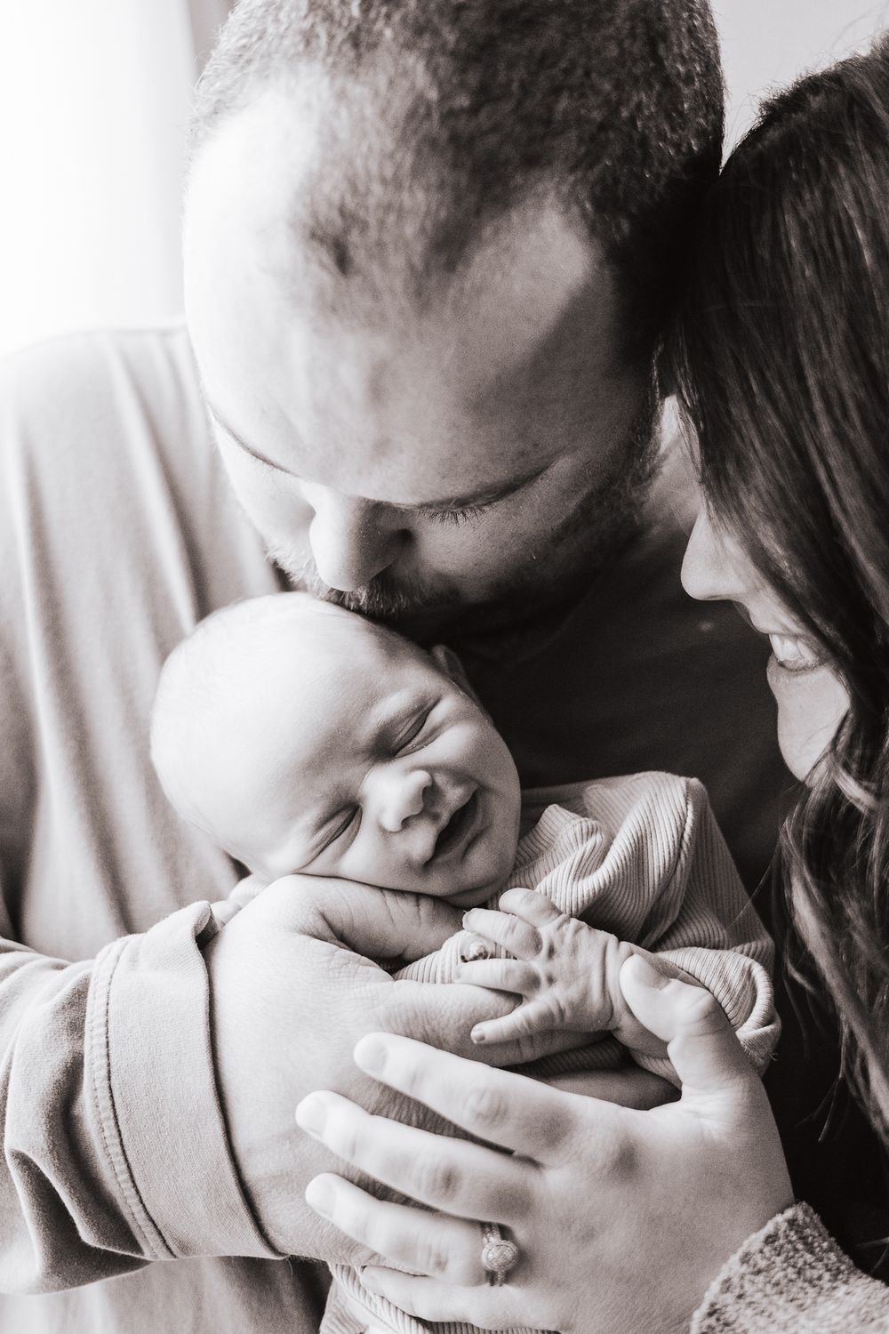 Intimate black and white portrait of parents cradling their sleeping newborn.
