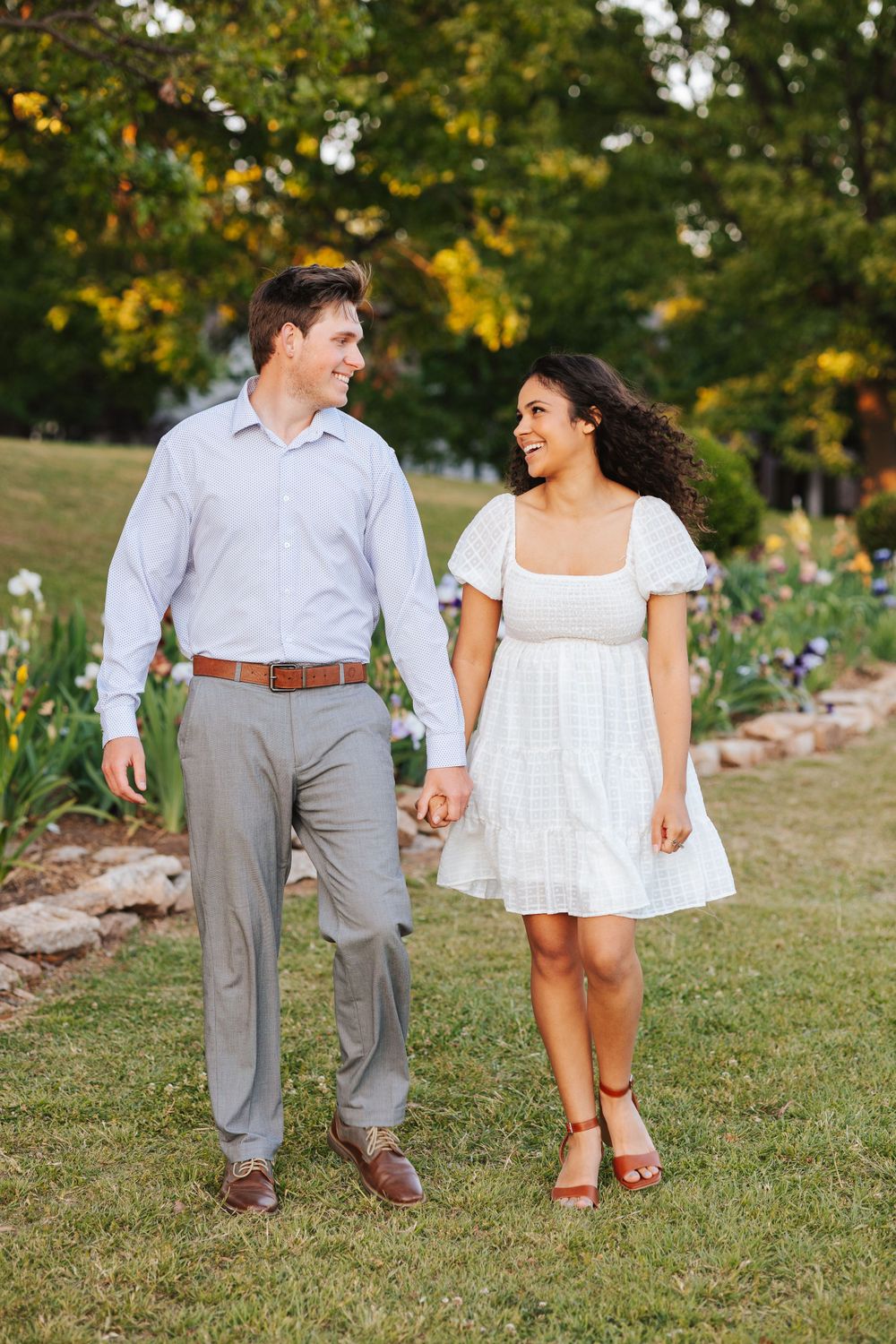 Couple walking together on grass path surrounded by garden flowers.