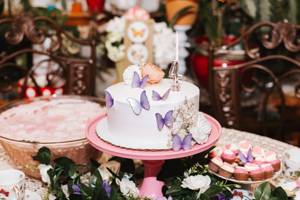 Elegant dessert table decorated with pink and white cakes, butterflies, and floral arrangements at a special event.