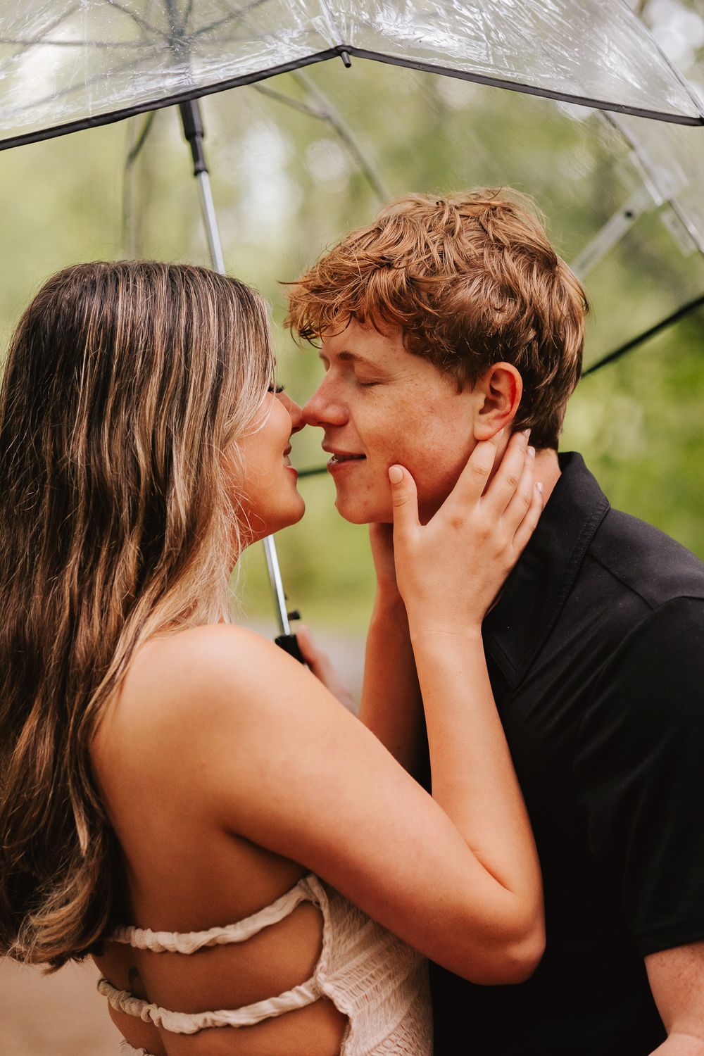 Romantic couple sharing intimate moment under clear umbrella in the rain.