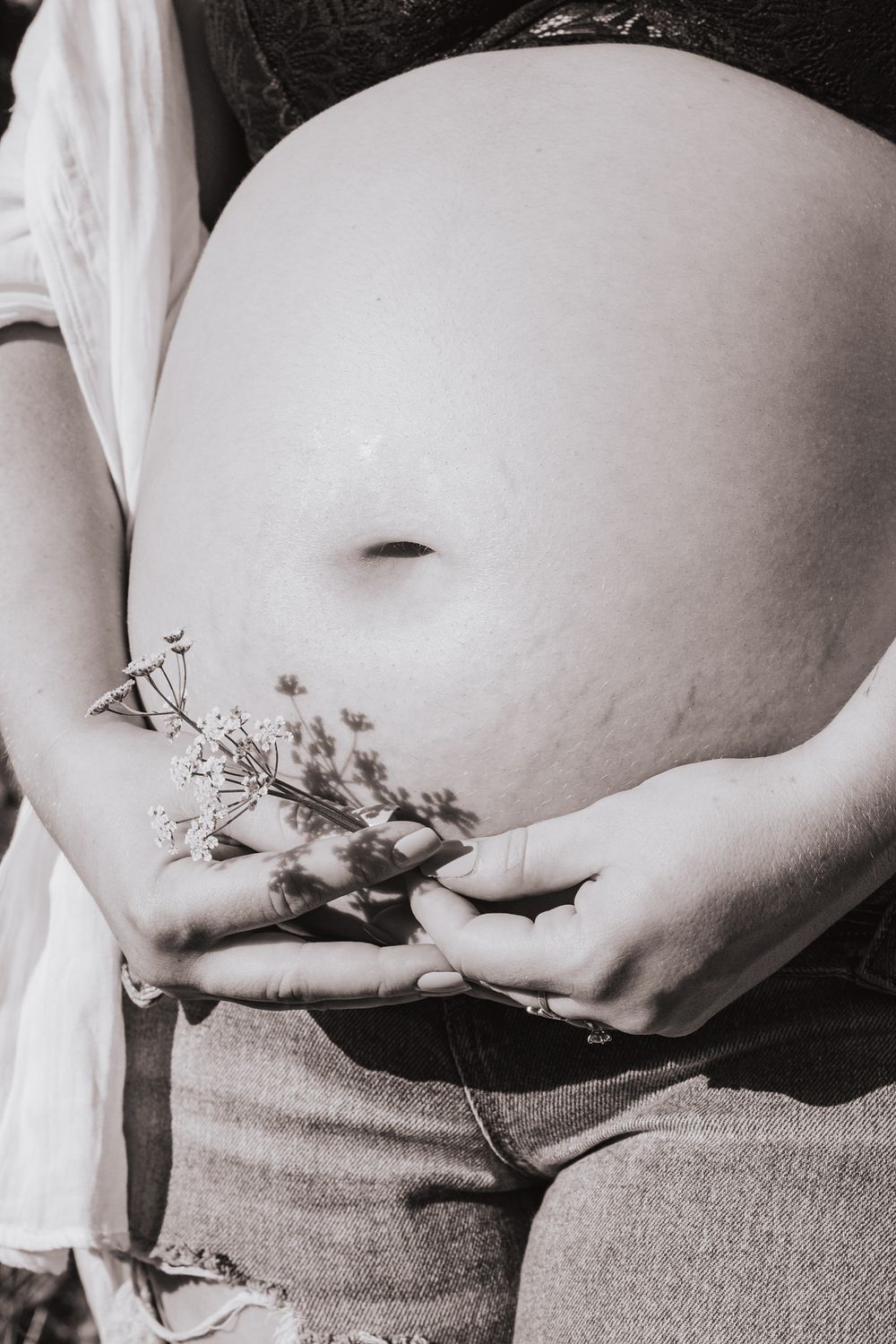 Black and white photos of a pregnant belly adorned with small flowers against a dark background.