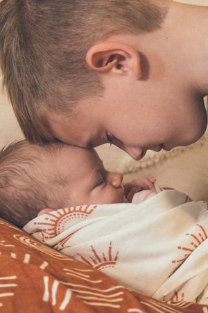 A sleeping child rests peacefully on a patterned pillow in warm lighting with older child touching foreheads.