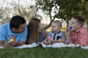 Family members lying on grass outdoors in a row taking playful photos together on a sunny day.
