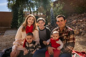 A family of five sits together outdoors on a sunny day wearing coordinated fall outfits.